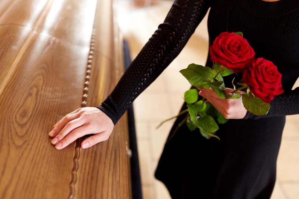 woman with red roses and coffin at funeral